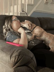 a woman laying on a couch with a dog licking her cheek