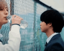 a man is drinking water from a bottle while standing next to another man .