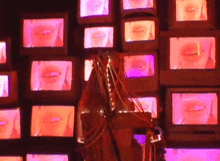 a woman is standing in front of a wall of televisions showing a woman 's mouths