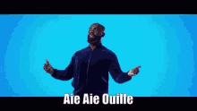 a man with a beard is standing in front of a blue background with the words aie aie quille on it .