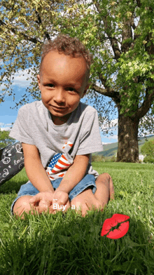 a little boy is sitting in the grass with a red flower and a sign that says " buy a "