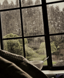 a bowl with a spoon in it sits on a window sill in front of a window that is covered in rain drops