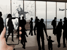 a hand is holding a cell phone with a picture of a group of people walking in front of a broken window