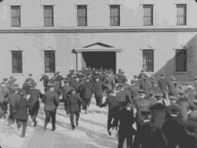 a black and white photo of a group of men running in front of a building that says 5th precinct police station