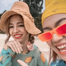 a woman wearing a straw hat and sunglasses smiles next to another woman wearing a bandana with the letter c on it