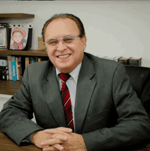 a man in a suit and tie is smiling in front of a bookshelf with a picture of a baby in a hat on it