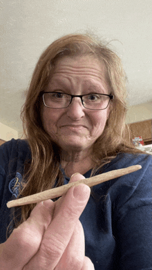 an older woman wearing glasses holds a cigarette in her hand