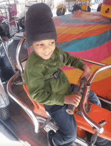 a young boy wearing a green sweater and a black beanie is sitting on a carousel