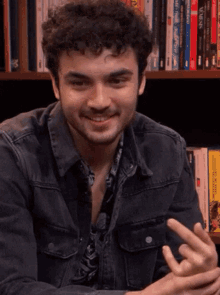 a man in a denim jacket is smiling in front of a bookshelf with a book titled venus on it