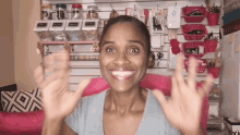 a woman in a grey shirt is smiling and waving her hands in front of a wall with baskets on it .