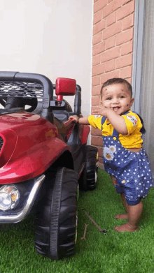 a baby is standing in front of a red jeep