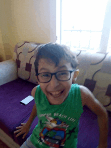 a young boy wearing glasses and a green shirt that says beach life smiles for the camera