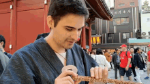 a man in a red shirt is eating a piece of food in front of a building with chinese writing on it