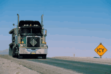 a large semi truck is driving down a road next to a sign that says icy