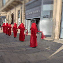 a group of people in red robes are walking in front of a debenham 's store