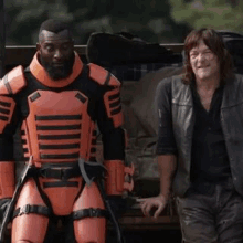 a man in a robot suit is standing next to a man in a black vest .