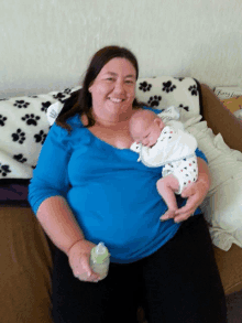 a woman in a blue shirt is holding a baby on a couch