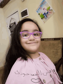 a girl wearing purple glasses and a pink shirt with arabic writing on it