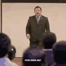 a man in a suit and tie is giving a presentation to a group of people in a classroom .