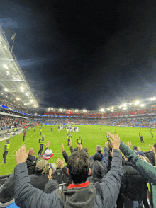 a soccer game is being played in a stadium with people raising their hands