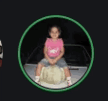 a little girl in a pink shirt is sitting on the back of a car .