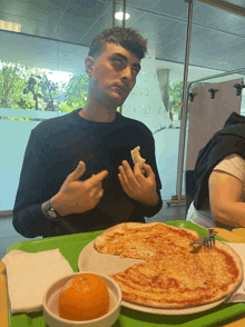 a man is sitting at a table with a pizza and an orange