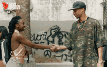 a man in a camo shirt shakes hands with a woman in front of a wall with graffiti on it that says word