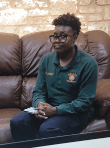 a woman wearing a green dallas shirt sits on a brown leather couch