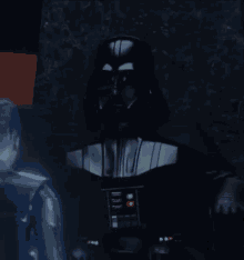 darth vader is standing in a dark room with a man standing behind him .