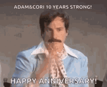 a man with a mustache is sitting at a table with his hands folded and a happy anniversary message .