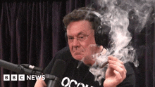 a man wearing headphones is smoking a cigar in front of a microphone that says bbc news