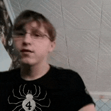 a young man wearing glasses and a black shirt with a spider and the number 4 on it .