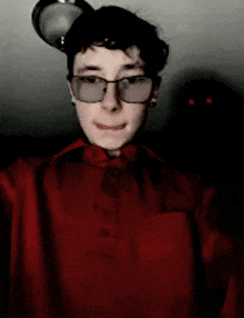 a young man wearing glasses and a red shirt is taking a selfie with a mouse on his head .