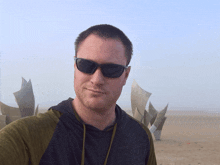 a man wearing sunglasses and a hoodie takes a selfie on the beach