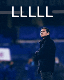 a man in a black jacket stands in front of a blue stadium with the letters lll on the bottom right