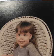 a little girl is sitting in a wicker chair and smiling