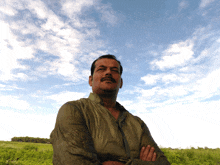 a man with his arms crossed stands in a field with a blue sky in the background