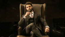 a man in a suit and tie is sitting in a chair and smoking a cigar .