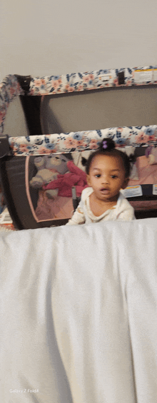 a little girl is standing in front of a crib with a teddy bear inside