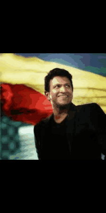 a man in a black suit and black shirt is smiling in front of a colorful flag .