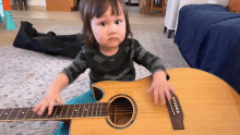 a little girl is playing an acoustic guitar while sitting on the floor