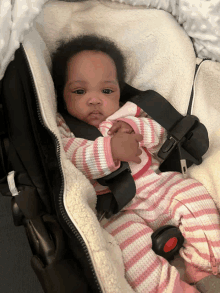 a baby is sitting in a car seat wearing a pink and white striped blanket