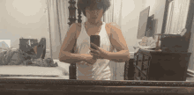 a man in a white tank top takes a selfie in a mirror