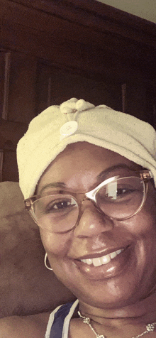 a woman wearing glasses and a towel turban smiles for the camera