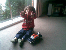 a young boy giving a thumbs up next to a toy