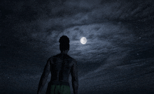 a man with dreadlocks stands in front of a full moon