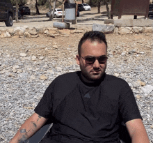 a man wearing sunglasses and a black adidas shirt sits on the rocks