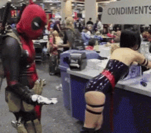 a man in a deadpool costume is standing next to a woman in a latex outfit in front of a condiments sign