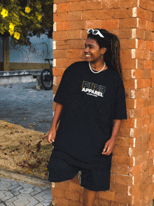 a woman leaning against a brick wall wearing a fire apparel t-shirt