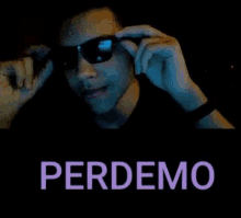 a man wearing sunglasses and a black shirt is talking on a cell phone in a dark room .